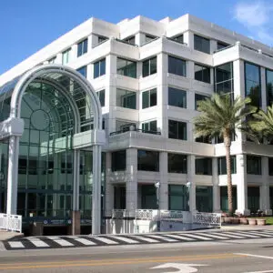 Modern office building with large glass windows, an archway entrance, and palm trees lining the exterior.