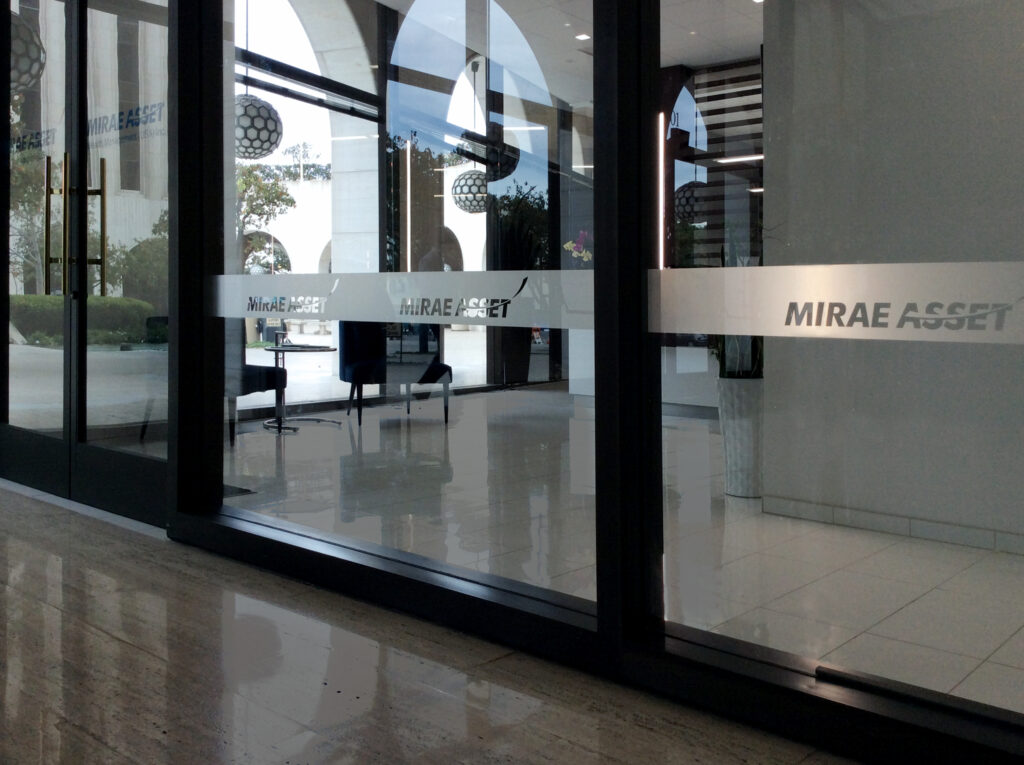 Glass entrance doors with frosted decals displaying "MIRAE ASSET," leading into a modern lobby with seating and large windows.